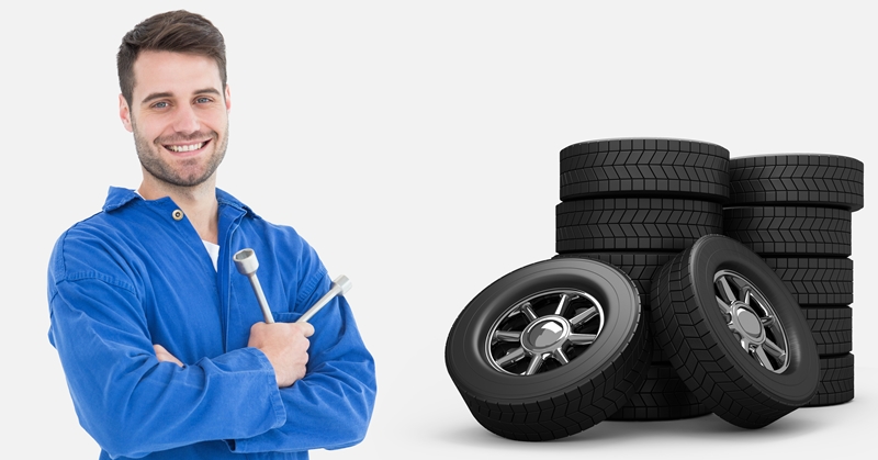 Smiling mechanic holding lug wrench and standing next to tyres